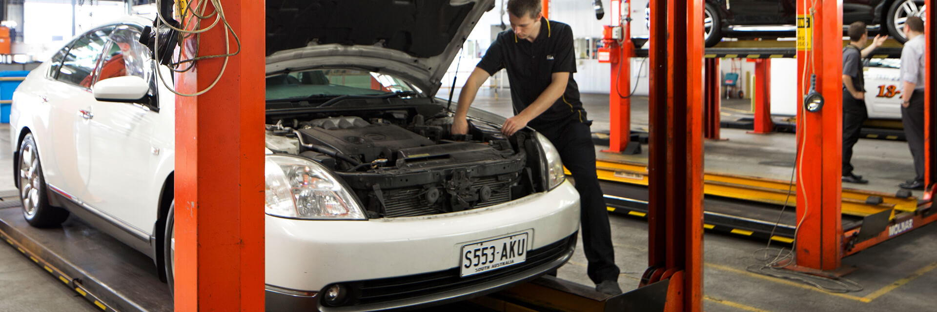 Car in workshop with bonnet open, a mechanic leans in to check the motor