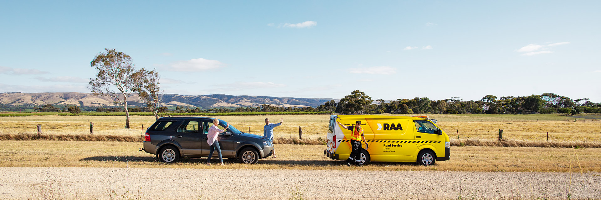 An RAA Road Service patrol van helping people with a car stopped on the side of the road.